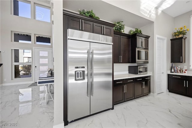 kitchen featuring a high ceiling, built in appliances, and dark brown cabinetry