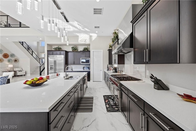 kitchen with decorative light fixtures, sink, a large island, built in appliances, and wall chimney exhaust hood