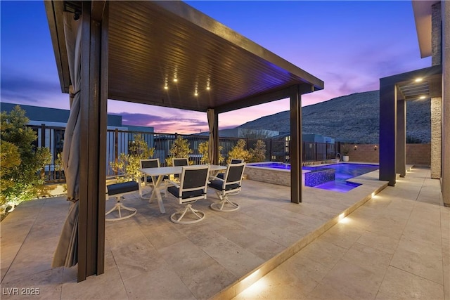 patio terrace at dusk featuring a mountain view and a pool with hot tub