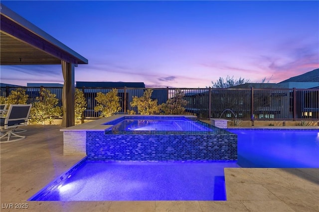 pool at dusk with an in ground hot tub, pool water feature, and a patio area