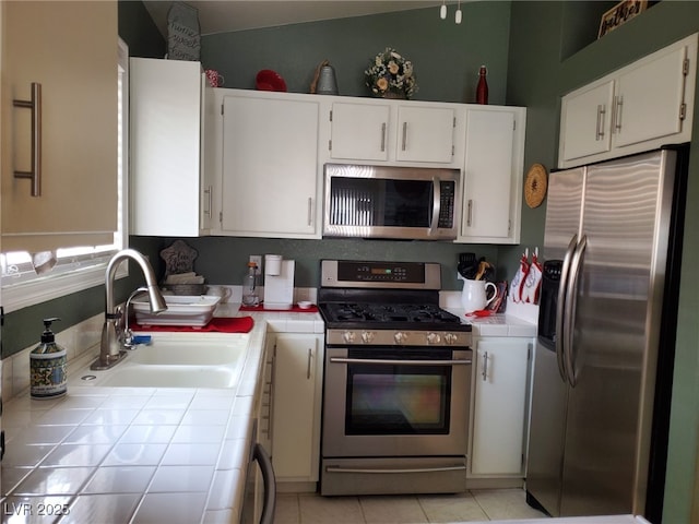 kitchen with white cabinetry, sink, tile counters, and stainless steel appliances