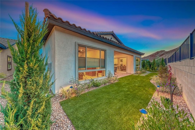 back house at dusk featuring a yard and a patio area