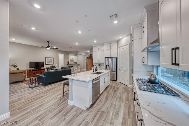 kitchen with sink, a breakfast bar area, appliances with stainless steel finishes, a kitchen island with sink, and white cabinets