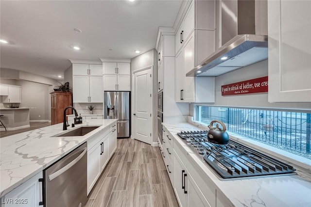 kitchen featuring sink, white cabinetry, appliances with stainless steel finishes, light stone countertops, and wall chimney range hood