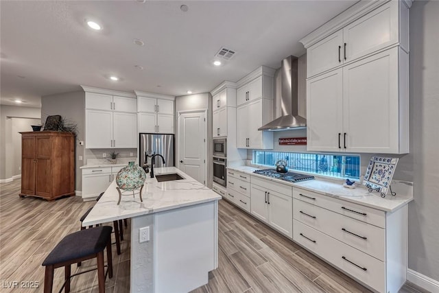 kitchen featuring an island with sink, white cabinetry, sink, stainless steel appliances, and wall chimney exhaust hood