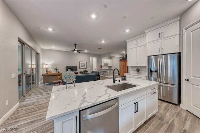 kitchen with sink, stainless steel appliances, white cabinets, and a center island with sink