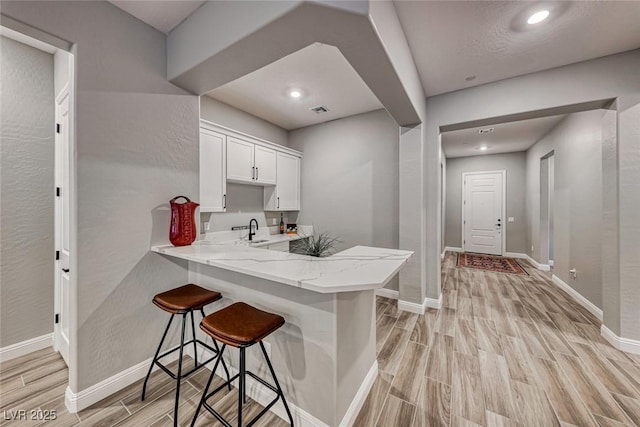 kitchen featuring white cabinetry, a kitchen breakfast bar, kitchen peninsula, and sink