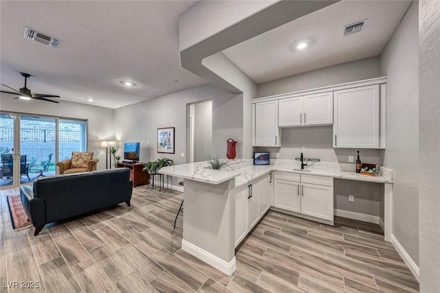 kitchen with ceiling fan, white cabinetry, light stone countertops, a kitchen bar, and kitchen peninsula