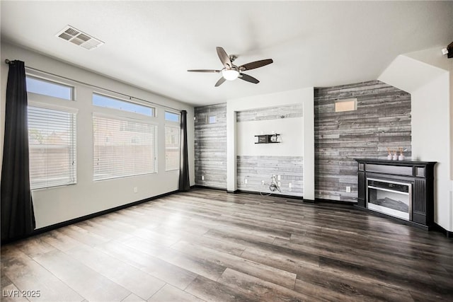 unfurnished living room featuring wood-type flooring, ceiling fan, and wooden walls