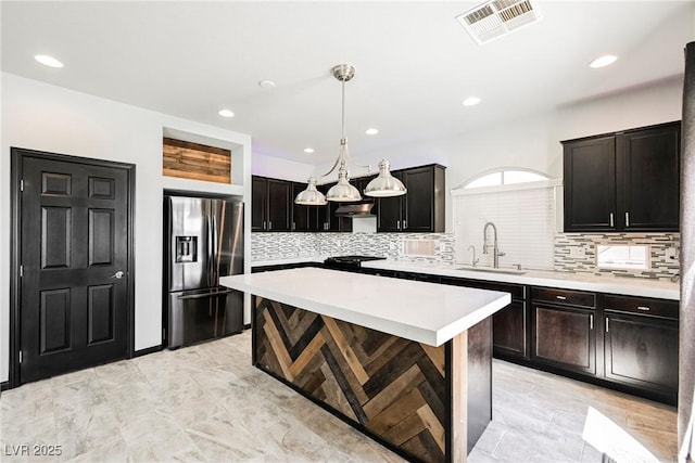 kitchen featuring a kitchen island, sink, backsplash, hanging light fixtures, and stainless steel refrigerator with ice dispenser