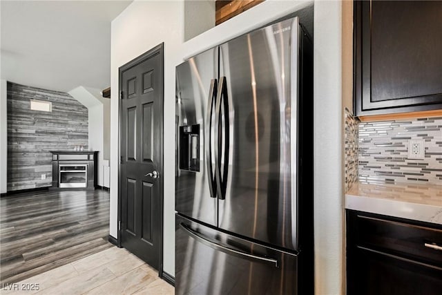 kitchen featuring tasteful backsplash, stainless steel refrigerator with ice dispenser, light hardwood / wood-style floors, and wood walls