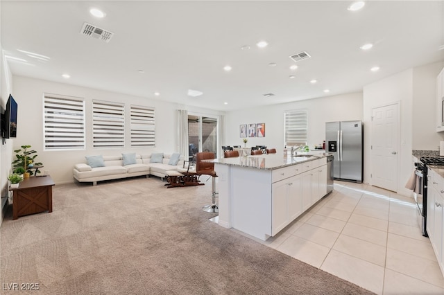 kitchen with stainless steel appliances, light stone countertops, an island with sink, white cabinets, and light carpet