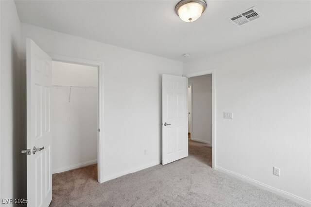 unfurnished bedroom featuring a walk in closet, light colored carpet, and a closet