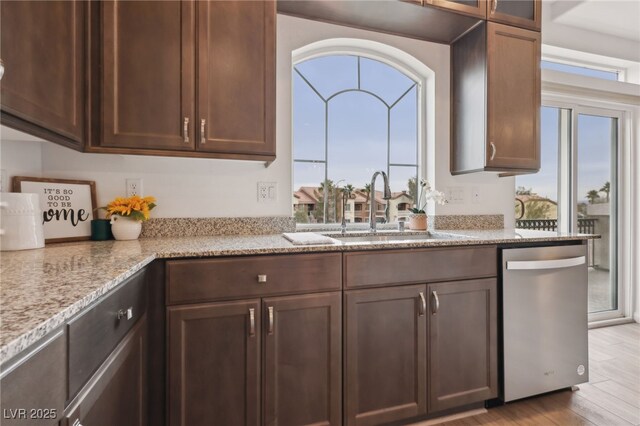 kitchen featuring dark brown cabinetry, sink, light wood-type flooring, stainless steel dishwasher, and light stone countertops