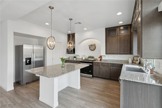 kitchen with sink, stainless steel appliances, a center island, and light stone countertops