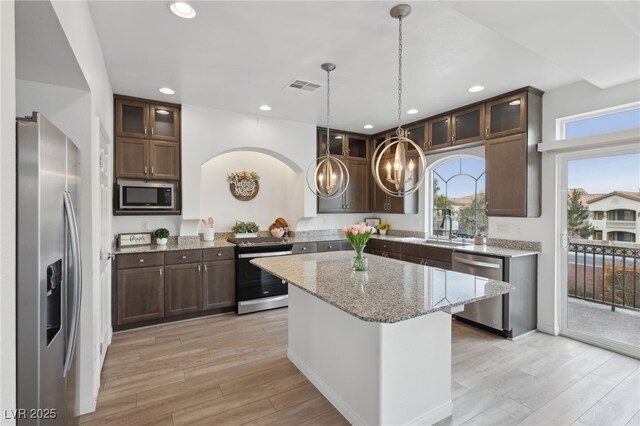 kitchen with pendant lighting, light hardwood / wood-style flooring, appliances with stainless steel finishes, light stone countertops, and a kitchen island