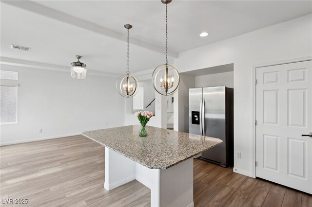 kitchen with stainless steel refrigerator with ice dispenser, a breakfast bar, light stone counters, hanging light fixtures, and light hardwood / wood-style floors