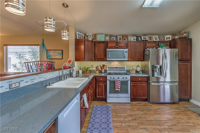 kitchen with pendant lighting, sink, hardwood / wood-style flooring, stainless steel appliances, and tasteful backsplash