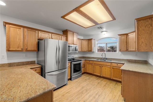 kitchen with stainless steel appliances, light stone countertops, sink, and light hardwood / wood-style flooring