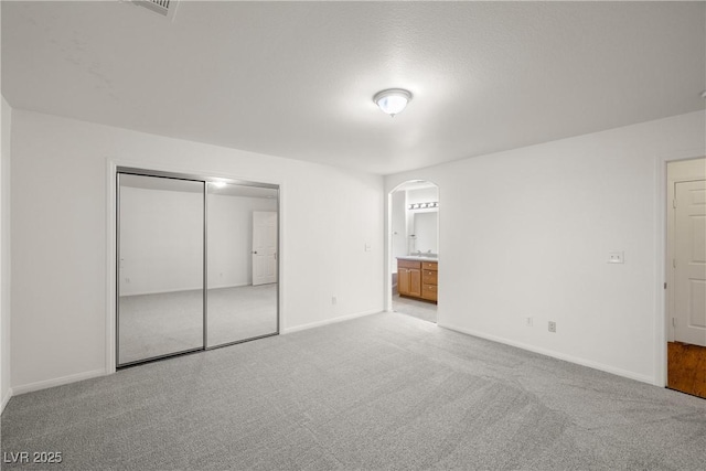 unfurnished bedroom with connected bathroom, light colored carpet, and a closet