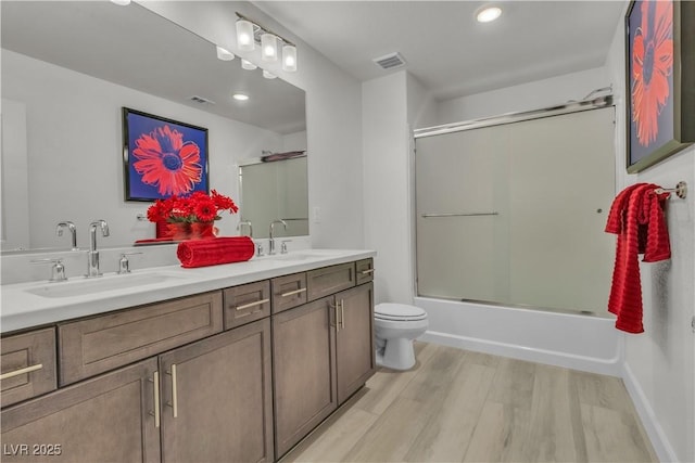 bathroom with double vanity, a sink, toilet, and wood finished floors