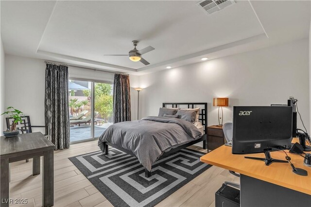 bedroom with light hardwood / wood-style flooring, access to outside, and a tray ceiling