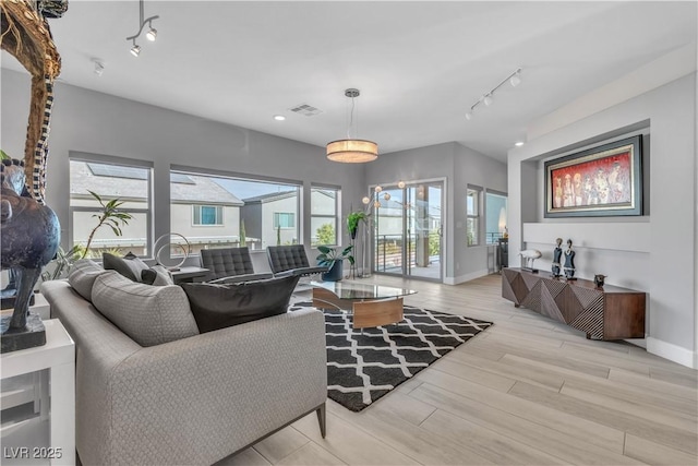 living room featuring light wood-type flooring, rail lighting, visible vents, and baseboards