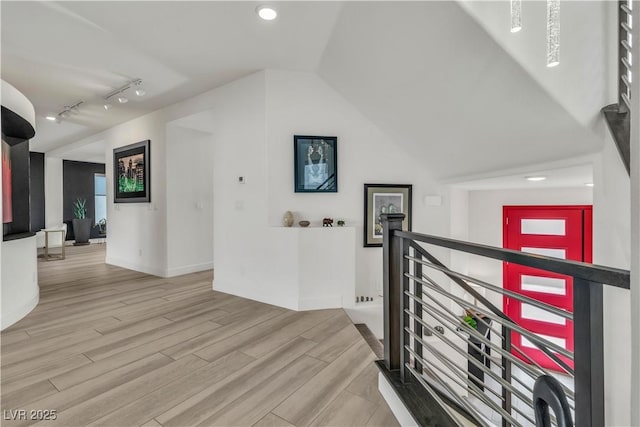 corridor with lofted ceiling, rail lighting, an upstairs landing, wood finished floors, and baseboards