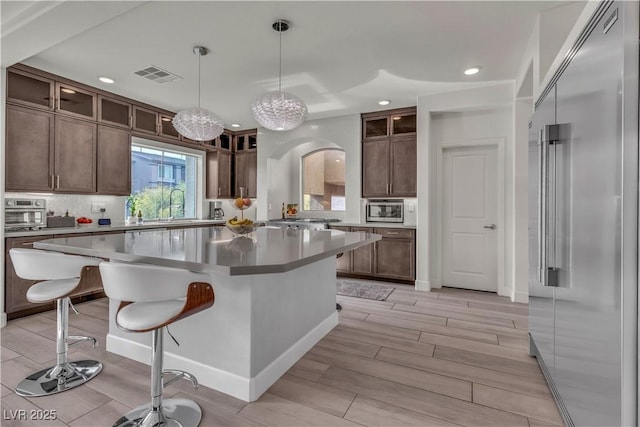 kitchen with a breakfast bar area, built in appliances, decorative light fixtures, a kitchen island, and backsplash