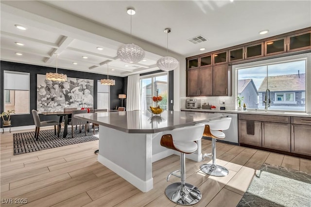 kitchen featuring dark brown cabinetry, a breakfast bar, sink, a kitchen island, and pendant lighting