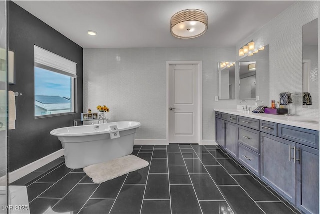 full bath with double vanity, baseboards, tile patterned floors, a freestanding bath, and a sink