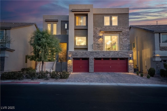 contemporary home with stone siding, decorative driveway, an attached garage, and stucco siding