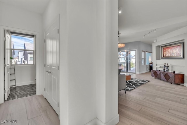 corridor with track lighting, baseboards, plenty of natural light, and light wood finished floors