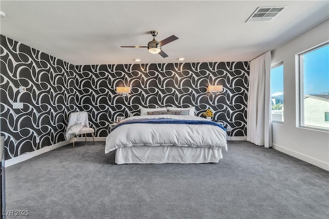 carpeted bedroom featuring wallpapered walls, baseboards, visible vents, a ceiling fan, and an accent wall