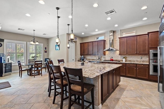 2920 Josephine Dr, Henderson, NV 89044 - kitchen with wall chimney exhaust hood, decorative backsplash, recessed lighting, an island with sink, and light stone countertops