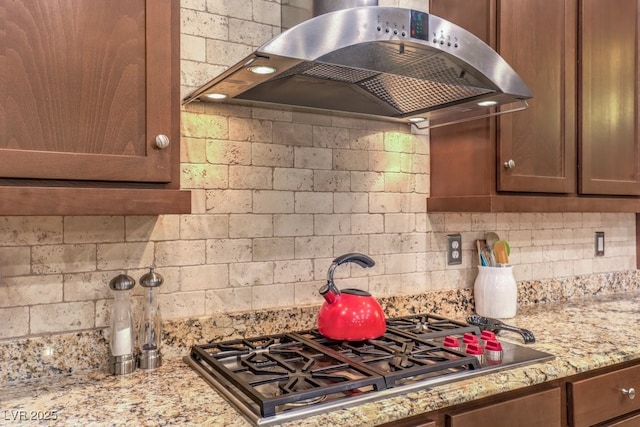 kitchen with tasteful backsplash, light stone countertops, exhaust hood, and stainless steel gas stovetop