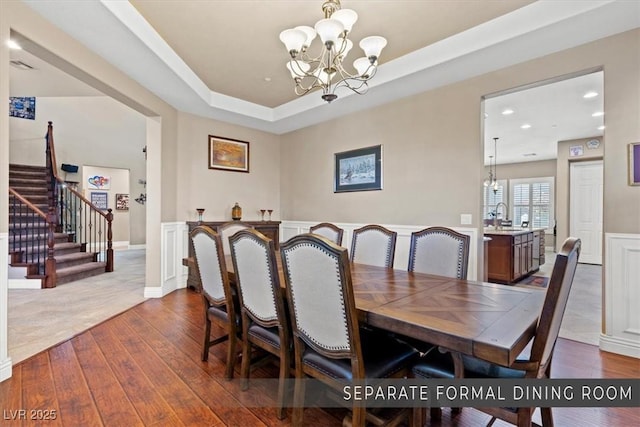 dining space featuring dark wood-type flooring, sink, a chandelier, and a tray ceiling