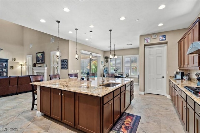 kitchen featuring sink, a kitchen island with sink, light stone counters, a high end fireplace, and decorative light fixtures