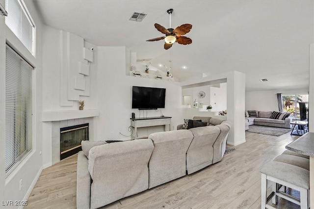 living room with ceiling fan, lofted ceiling, a tiled fireplace, and light hardwood / wood-style flooring