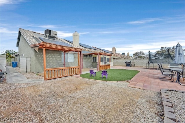 rear view of property with a trampoline, cooling unit, a yard, a patio, and solar panels