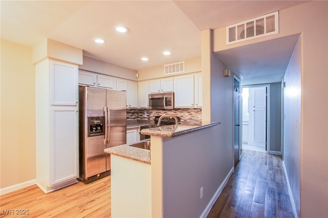 kitchen with appliances with stainless steel finishes, tasteful backsplash, white cabinets, kitchen peninsula, and light hardwood / wood-style flooring