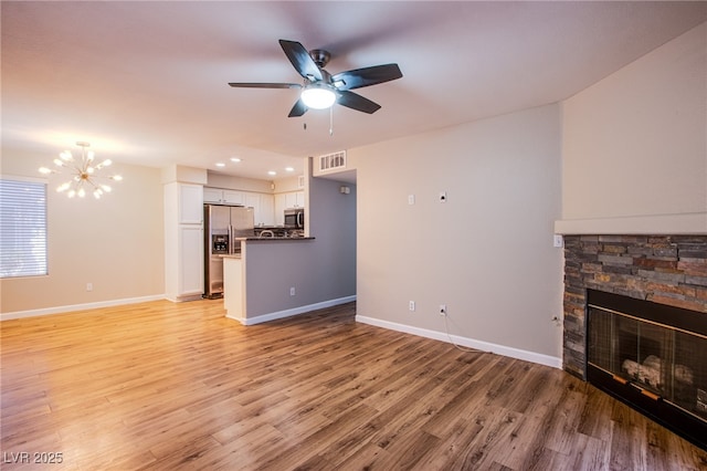 unfurnished living room featuring a stone fireplace, ceiling fan with notable chandelier, and light wood-type flooring