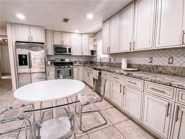 kitchen with sink, light tile patterned floors, appliances with stainless steel finishes, backsplash, and light stone countertops