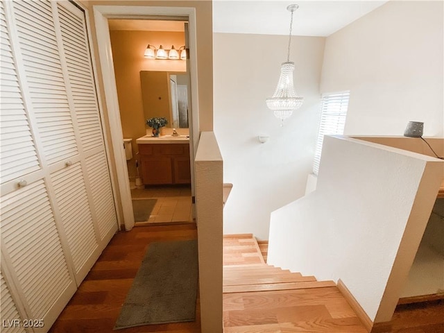 stairway with wood-type flooring, sink, and a notable chandelier