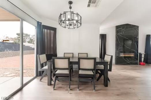 dining area with a premium fireplace, lofted ceiling, hardwood / wood-style floors, and a chandelier