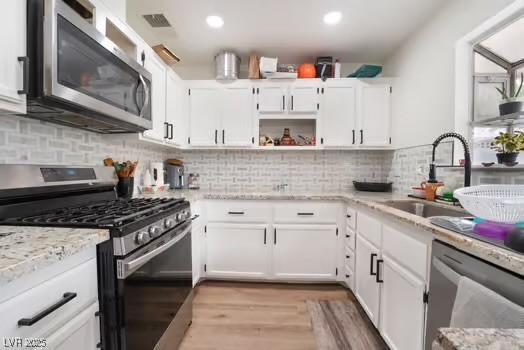 kitchen featuring appliances with stainless steel finishes, sink, backsplash, white cabinets, and light stone counters