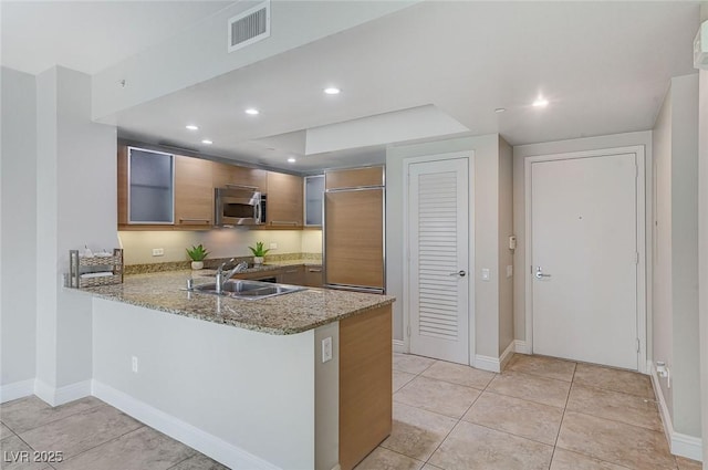 kitchen featuring sink, paneled built in refrigerator, light tile patterned floors, light stone counters, and kitchen peninsula