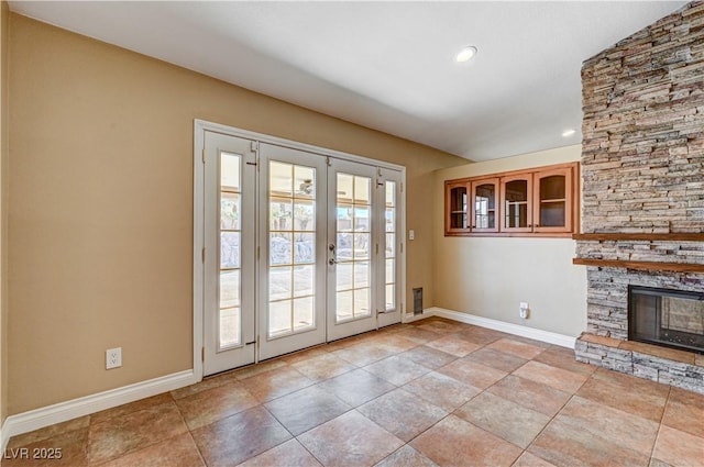 entryway with light tile patterned floors, a stone fireplace, and french doors