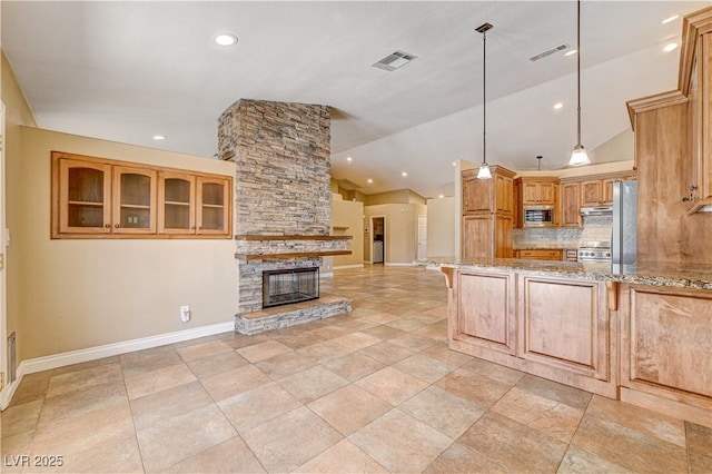 kitchen featuring lofted ceiling, appliances with stainless steel finishes, a fireplace, light stone countertops, and decorative light fixtures