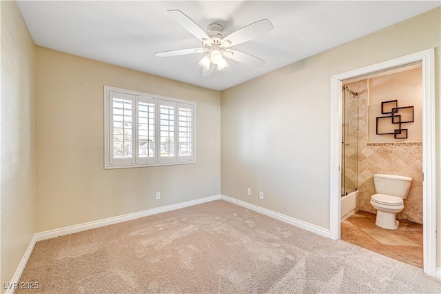 unfurnished bedroom featuring ceiling fan, ensuite bathroom, light carpet, and tile walls